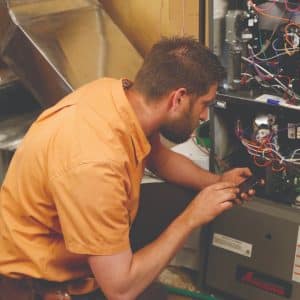 Professional furnace repair technician performing a seasonal maintenance check on a home heating system.